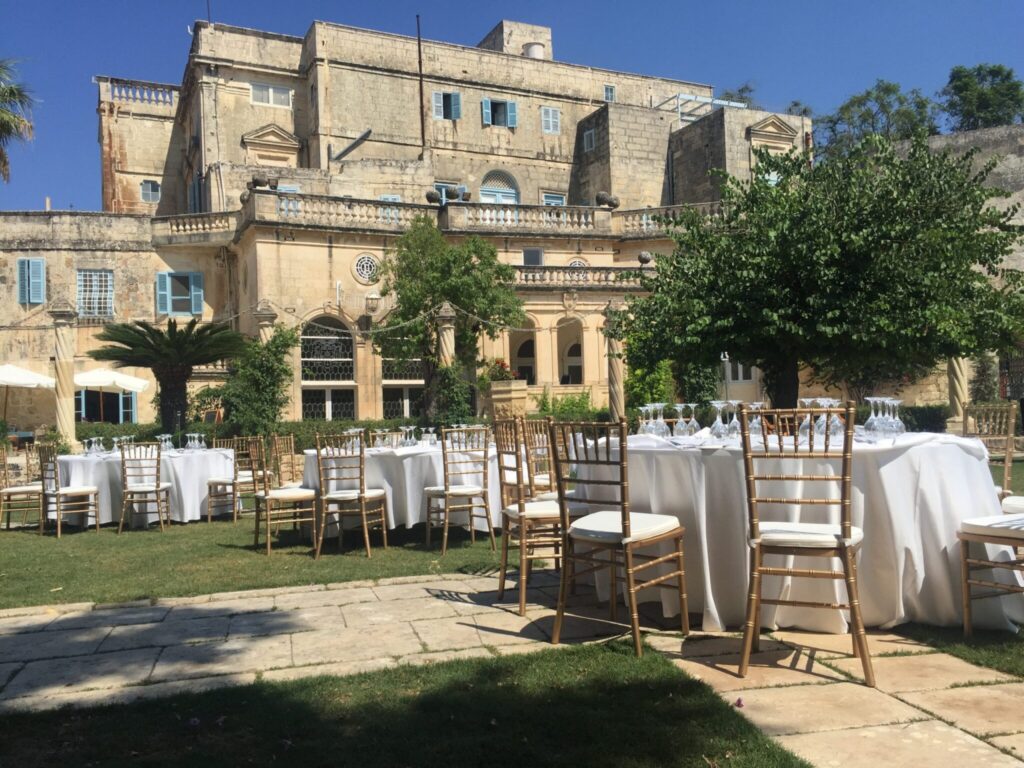 The image shows an outdoor event setup in the gardens of Villa Bologna, a historic 18th-century aristocratic villa in Attard, Malta.